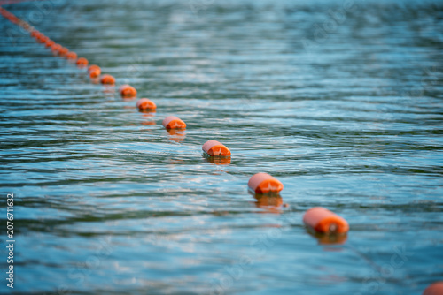 Fotografie A diagonal row of bright safety floats on a calm river disappearing into a blurry background, concept of security and water boundaries