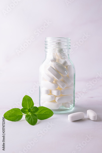 White medical capsules in glass jar decorated with fresh green leaves. Natural vegan medicine concept. Organic medical capsules.