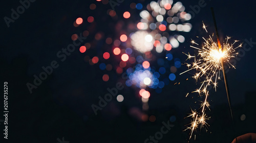 Sparkler firework celebration night bokeh sparkle Burning sparkler glowing bright beside colorful firework bokeh dark night sky, festive celebration background with warm light, excitement