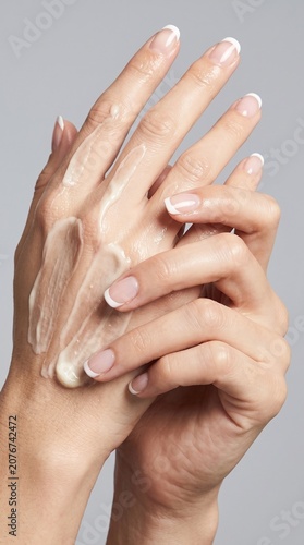 Woman applying moisturizing cream onto her hands with french manicure nails