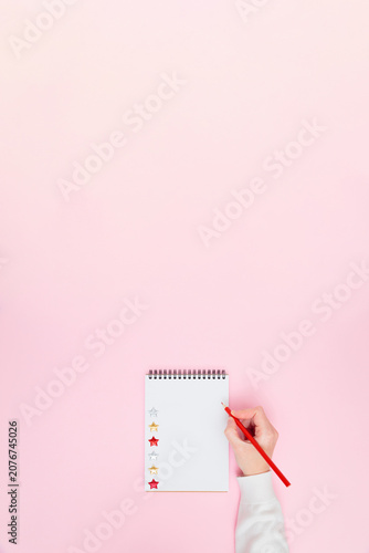Female hand writing on blank notebook with stars on pastel pink background, flat lay vertical banner with copy space for planning, goals, wish list, creative work, business or education concept.
