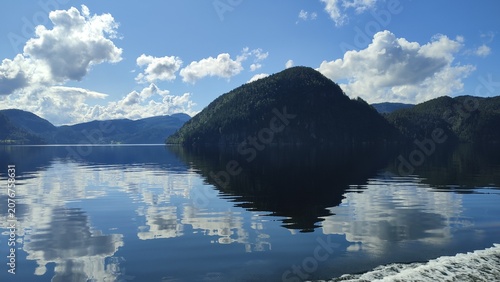 Valokuva Peaceful Norwegian fjord with mirror-like reflections of forested mountains and clouds on calm water during a sunny summer day
