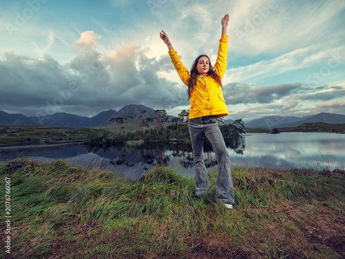 Obraz na płótnie Young woman in yellow jacket stands near calm lake