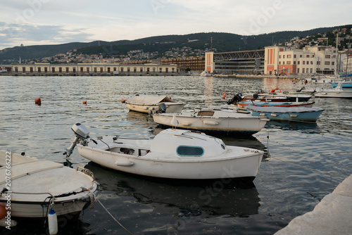 Fotografie Small motor boats and skiffs moored in a city harbor with port buildings and gre