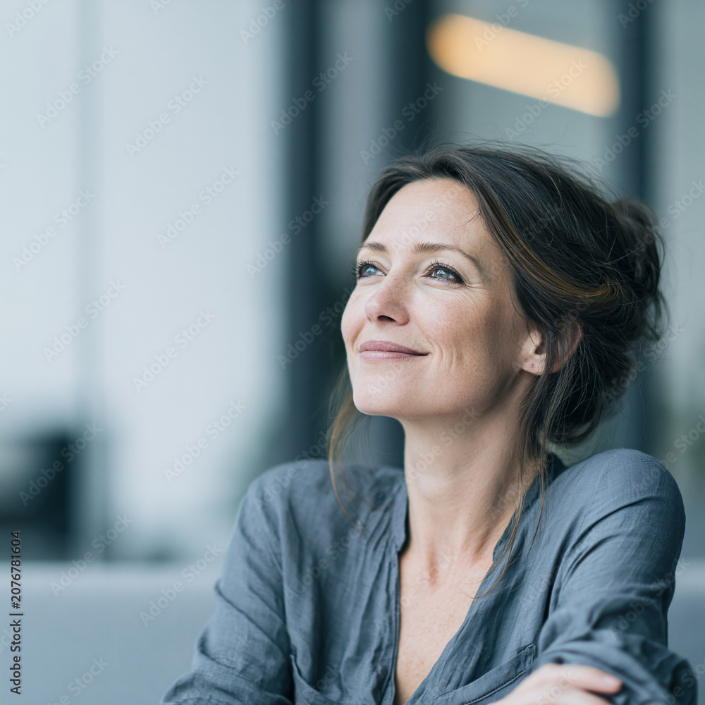 Obraz premium smiling female cio executive looking up in modern technology office, confident technology executive smiling across modern glass workplace, mature female business leader