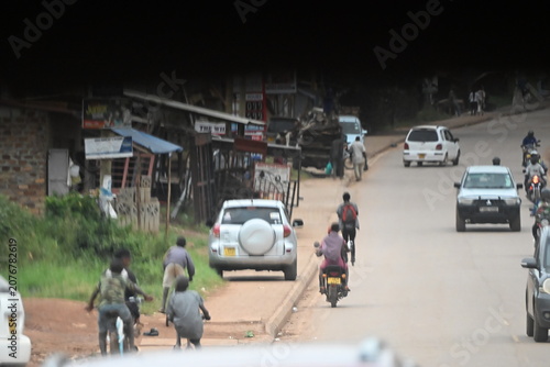 A journey along the roads of Uganda, passing through busy cities, small towns, and rural villages. The scene captures everyday traffic, motorcycles, cars, buses, pedestrians, roadside shops, and local