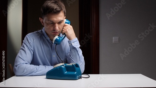 Foto Man intently listening to a conversation on a retro blue rotary telephone