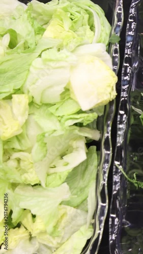 Top view of catering salad bar ingredients featuring fresh green lettuce leaves in a glass bowl, chopped herb greens in a black container, and sliced red onion rings on a black table.