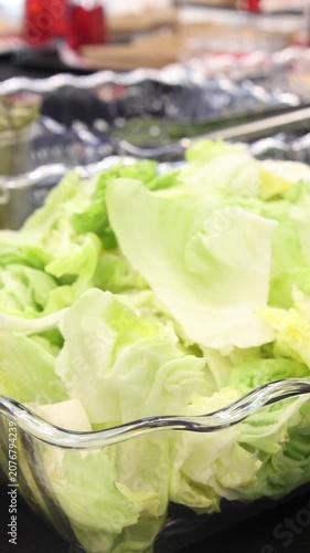 Close-up of green lettuce leaves in a clear scalloped glass bowl on a black catering table with ample copy space representing healthy organic salad for a festive buffet event party banquet serving.