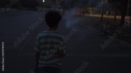 Young boy watching a firecracker explode on the street at dusk, celebrating the 4th of july in a suburban neighborhood with family enjoying the festive pyrotechnics