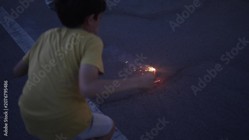 Children lighting small fireworks fountain on asphalt parking lot during twilight celebration, sparks flying and smoke creating a festive and exciting atmosphere for boys