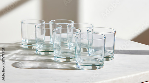 Set of clear empty drink glasses on a white countertop with natural light and shadow play, ready for beverage service