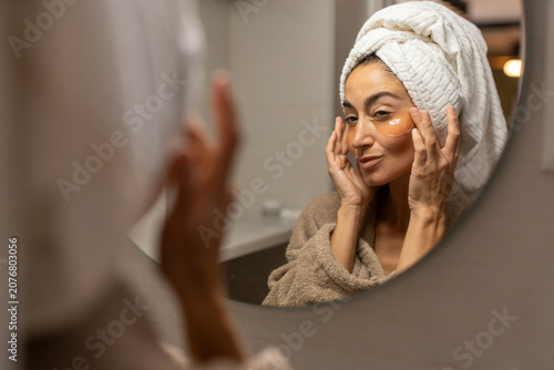 Woman applying hydrogel under eye patch during evening skincare routine at home bathroom focused on hydration anti aging treatment beauty wellness and facial self care concept