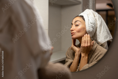 Фотография Adult woman massaging moisturizing facial cream into skin while standing at bath