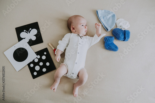 Cute 1 month baby boy lying among various playful colorful toys on beige blanket. Newborn surrounded by vivid objects participating actively in sensory exploration and learning. 