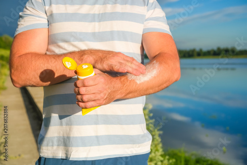 Obraz na plátně Man applies sunscreen cream to forearm near lake in summer