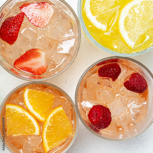 Colorful fruit infused sparkling drinks with ice cubes in glasses top view summer refreshment set