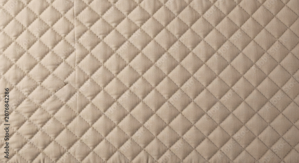Fototapeta premium Quilted fabric texture with diamond pattern in light beige color showing soft textile material for luxury bedding or upholstery design