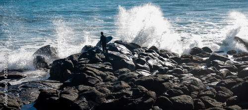 A surfer enters the water near Raglan New Zealand as waves crash around him