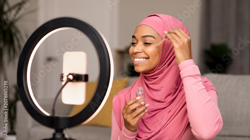 Fotografie Smiling Young Black Woman Applying Hydrating Skincare Serum In Front Of Mirror At Home, Demonstrating Self-care Routine, Feeling Confident And Happy While Taking Care Of Skin