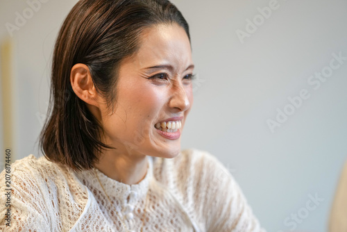 Young woman smiles warmly, eyes slightly closed. Soft lighting highlights her calm, joyful expression. She wears a cozy, textured white sweater. Ideal for lifestyle, wellness