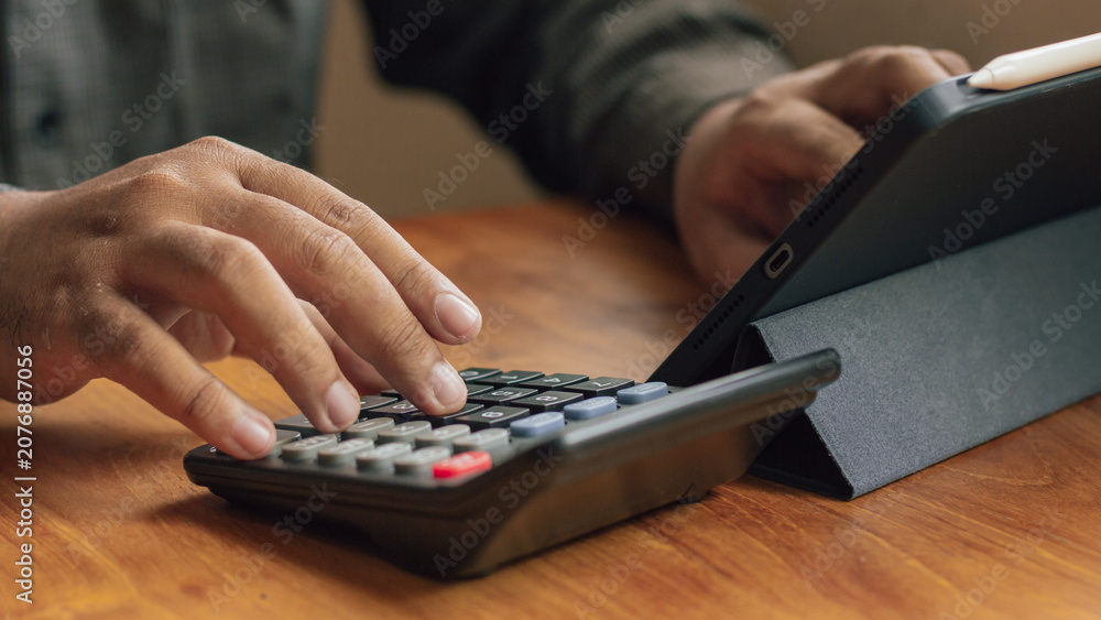 Fototapeta premium Close Up of Hands Using A Calculator and Tablet on Wooden Desk