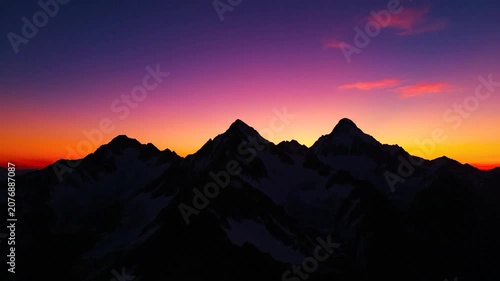 Silhouette of jagged mountain peaks against colorful sunset sky.