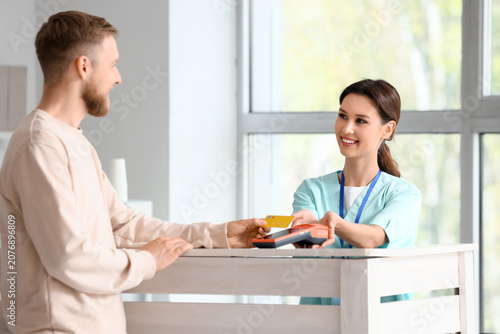 Cuadro en lienzo Female receptionist receiving payment from patient via terminal in clinic