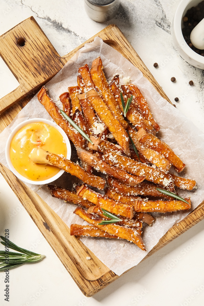 Obraz premium Wooden board with tasty cooked sweet potato, grated Parmesan cheese, rosemary and bowl of sauce on marble background