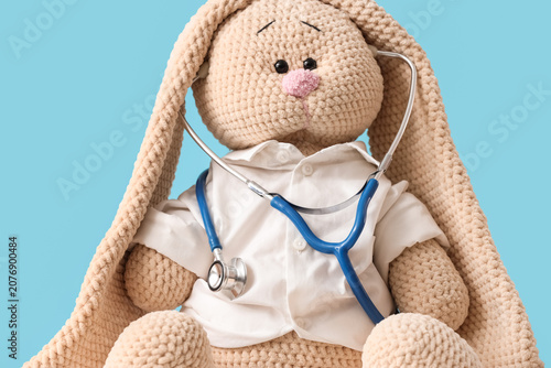 Toy bunny with stethoscope dressed as pediatrician on blue background, closeup