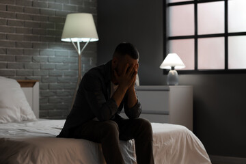 Depressed young man sitting in bedroom. International Stress Awareness Week