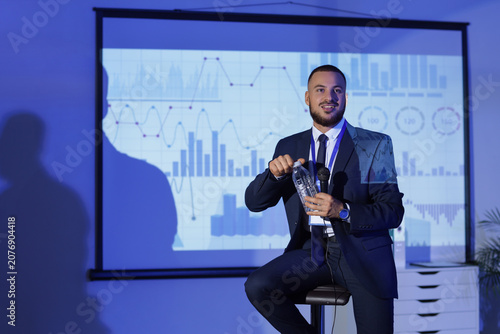 Male business speaker with water bottle conducting seminar near projector scr...