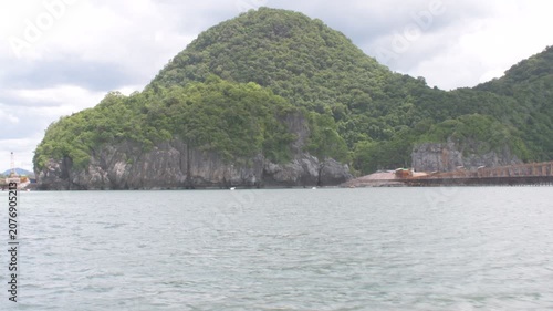 approaching the scenic khanom coastline in southern thailand, featuring a lush limestone hill, calm gulf waters, and dramatic tropical shoreline under a cloudy sky