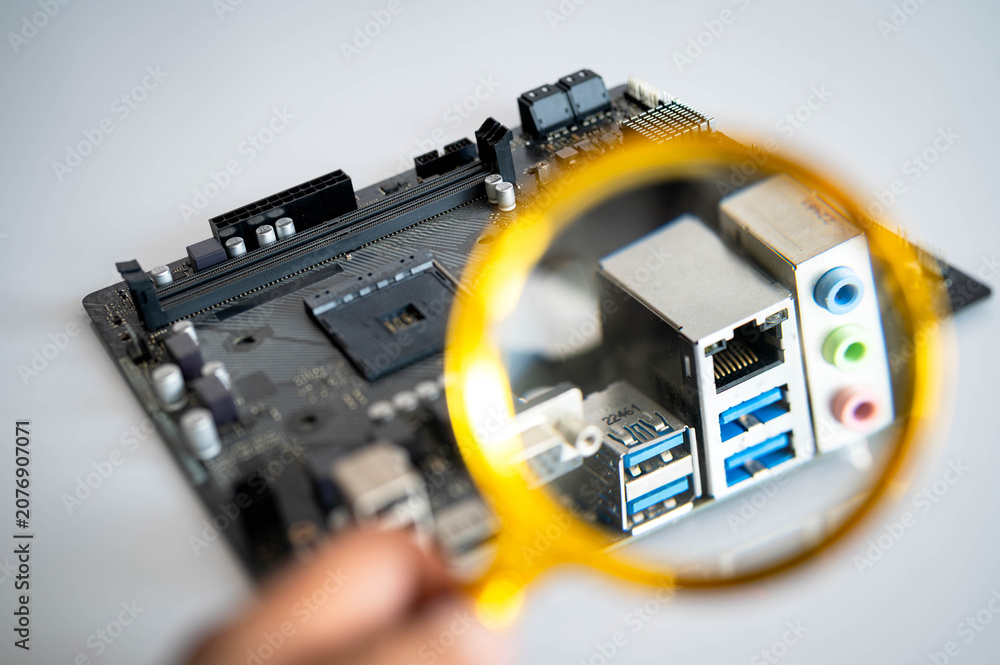 Fototapeta premium Magnifying glass inspecting motherboard rear I/O ports, highlighting computer hardware, connectivity and electronic interface. Concept of technology diagnostics, quality inspection.