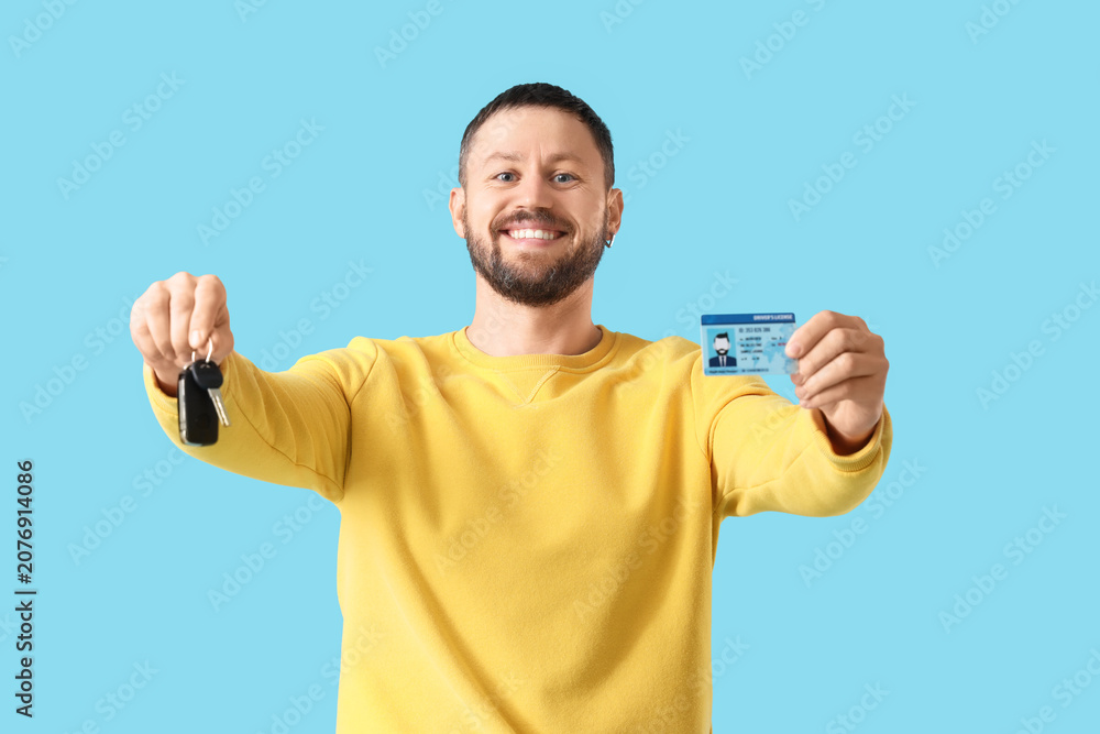 Fototapeta premium Young man with driving license and car key on blue background