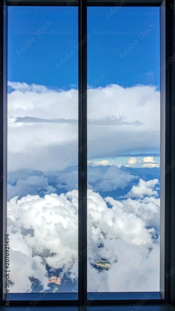 Fototapeta premium Framed view of blue sky and billowing white clouds seen through a glass window