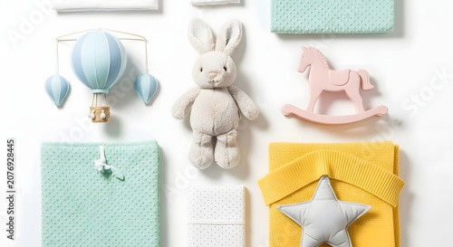 A flat lay arrangement of soft pastel baby nursery items including a stuffed bunny, hot air balloon mobile, rocking horse, and blankets.