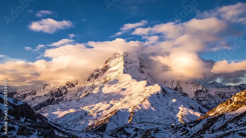 Symmetrical morning glow on a majestic snow capped mountain peak with clouds moving in a cinematic time lapse