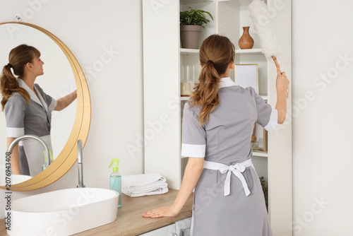 Konstfotografi Young chambermaid cleaning shelf with pp-duster in bathroom