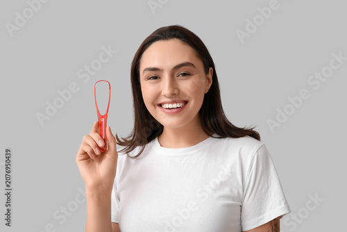 Young woman with tongue scraper on light background, closeup