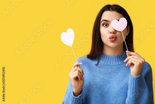 Beautiful young girl with paper hearts on yellow background. Valentines Day c...