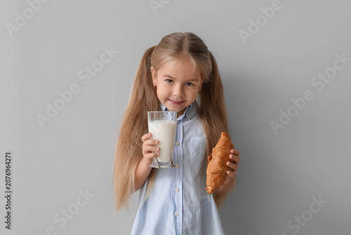 Tableau sur toile Cute little girl with glass of tasty milk and croissant on grey background
