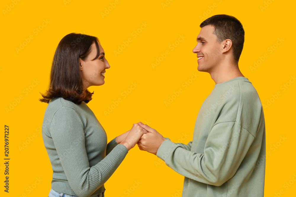 Fototapeta premium Happy young couple holding hands and smiling at each other on yellow background