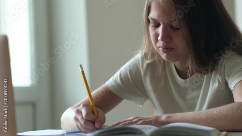 Bored and tired teenage girl crying while doing homework. Schoolgirl unhappy in her studying