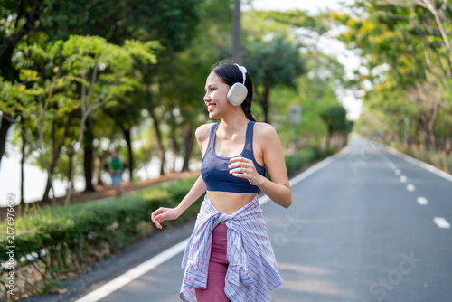 Asian sportswoman wearing headphones while running exercise in garden.