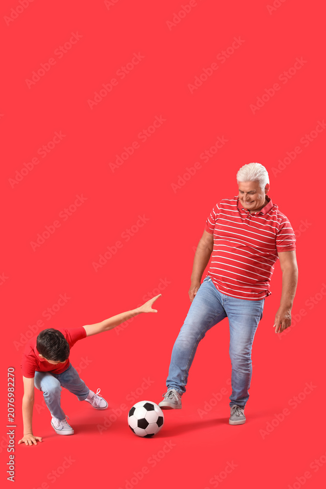 Obraz premium Little boy with his grandfather playing football on red background