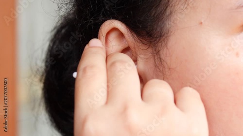 Close up of a young Asian woman cleaning her ear with a cotton swab for personal healthcare and ear disease prevention.