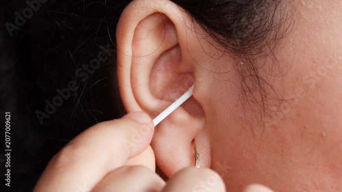 Close up of a young Asian woman cleaning her ear with a cotton swab for personal healthcare and ear disease prevention.