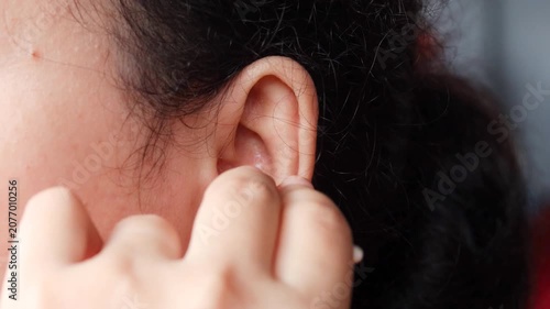 Close up of a young Asian woman cleaning her ear with a cotton swab for personal healthcare and ear disease prevention.