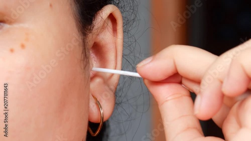 Close up of a young Asian woman cleaning her ear with a cotton swab for personal healthcare and ear disease prevention.